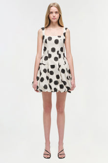 White sleeveless mini dress with black polka dot pattern and gathered skirt hem.