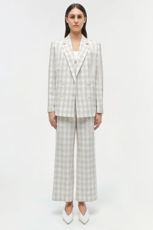 Woman wearing a light gray and white checkered double-breasted blazer with matching wide-leg trousers and white pointed-toe b
