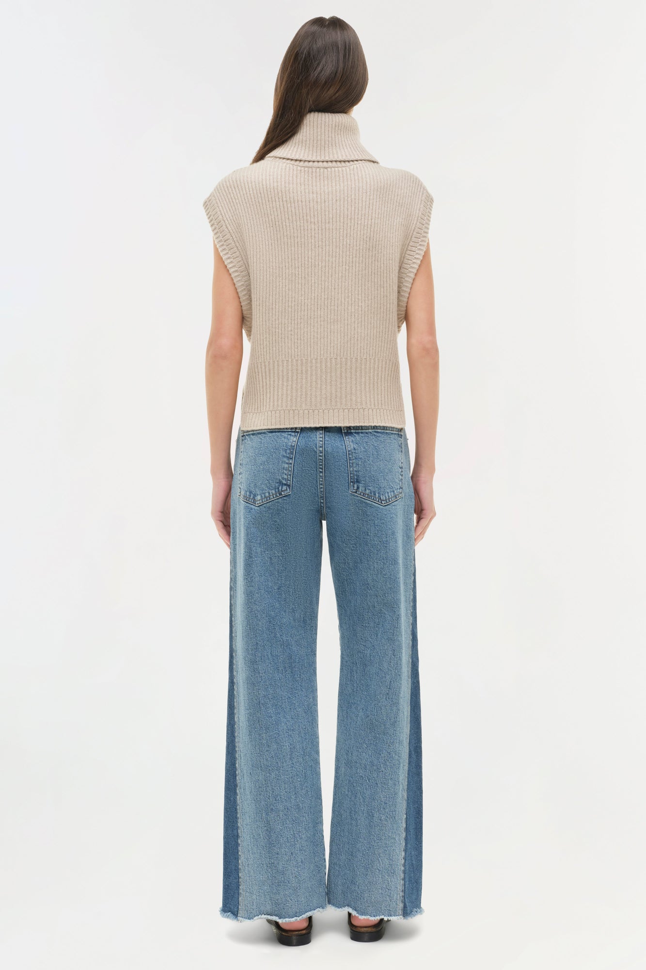 Blue straight leg jeans with frayed hem, shown from behind with cream sleeveless turtleneck.