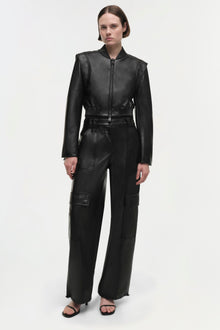 Woman wearing black leather cropped jacket with ribbed collar and cuffs, paired with matching cargo pants.