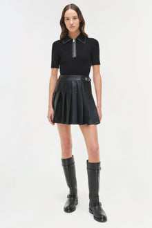 Black knit mini dress with collared polo top, half-zip closure, pleated leather skirt, and buckle belt detail.