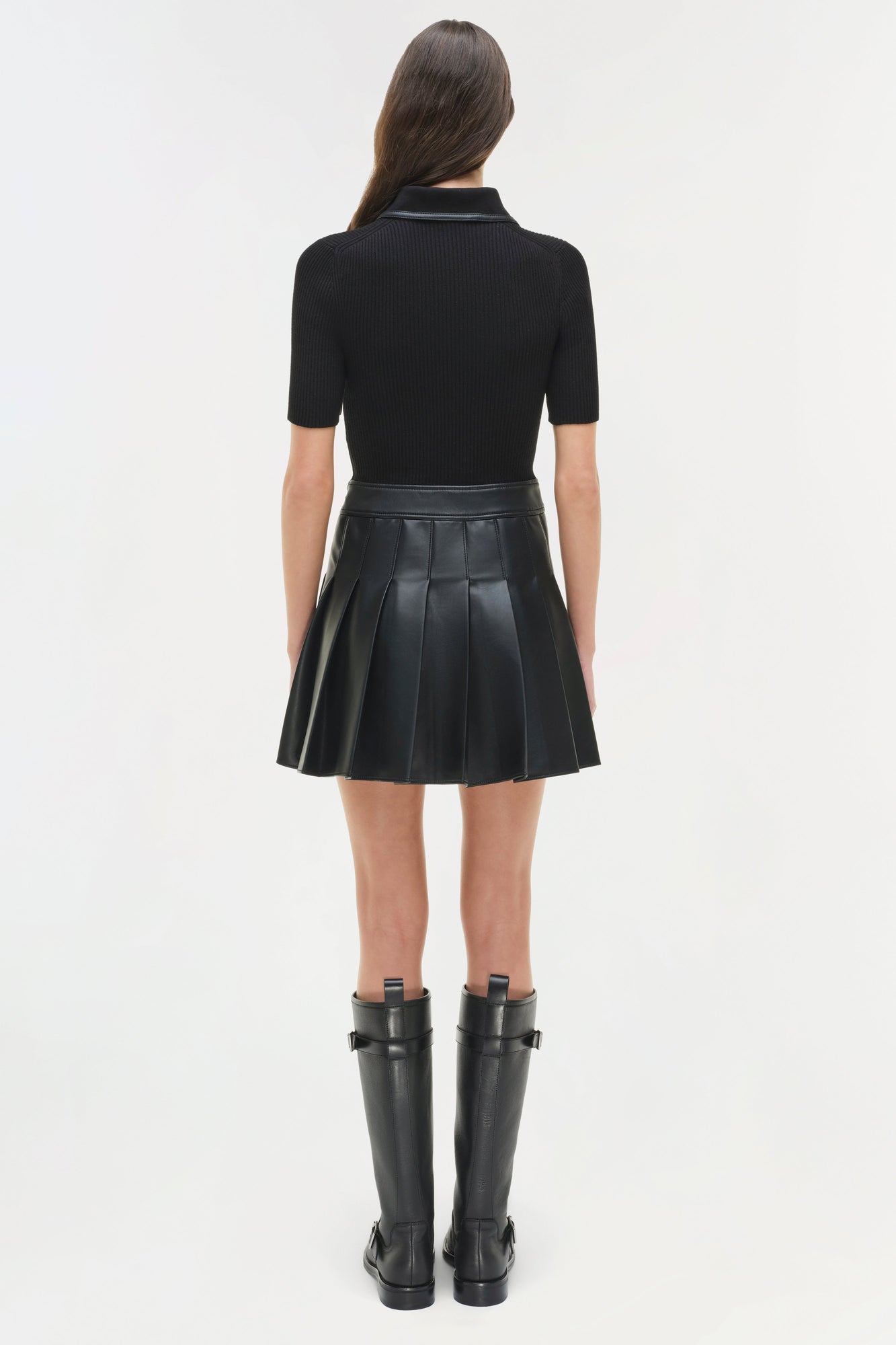 Black mini dress with ribbed knit collared top and pleated leather skirt, worn with black knee-high boots.