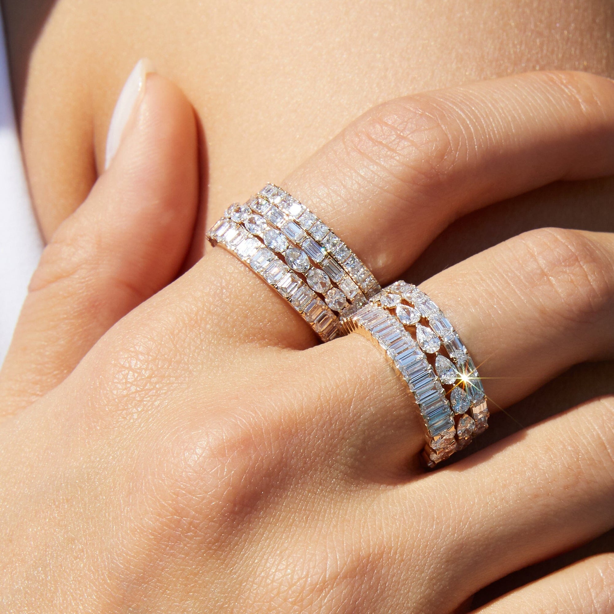 Model Close-up of a woman's hand resting against her chest, wearing multiple stacked gold and diamond eternity rings featuring mixed cuts, including baguette and pear shapes