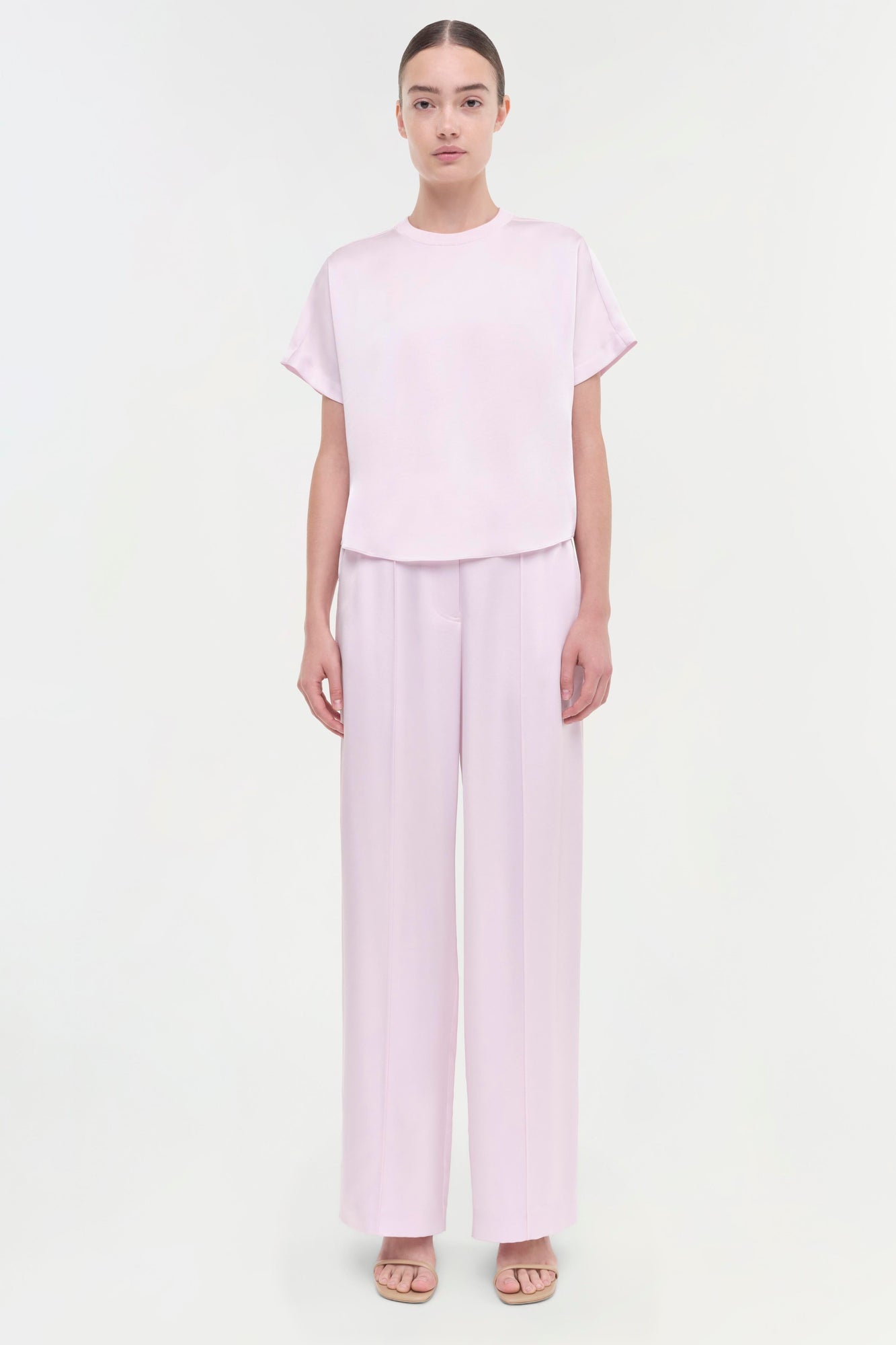 Woman wearing light pink short-sleeve t-shirt and matching wide-leg pants with slide sandals.