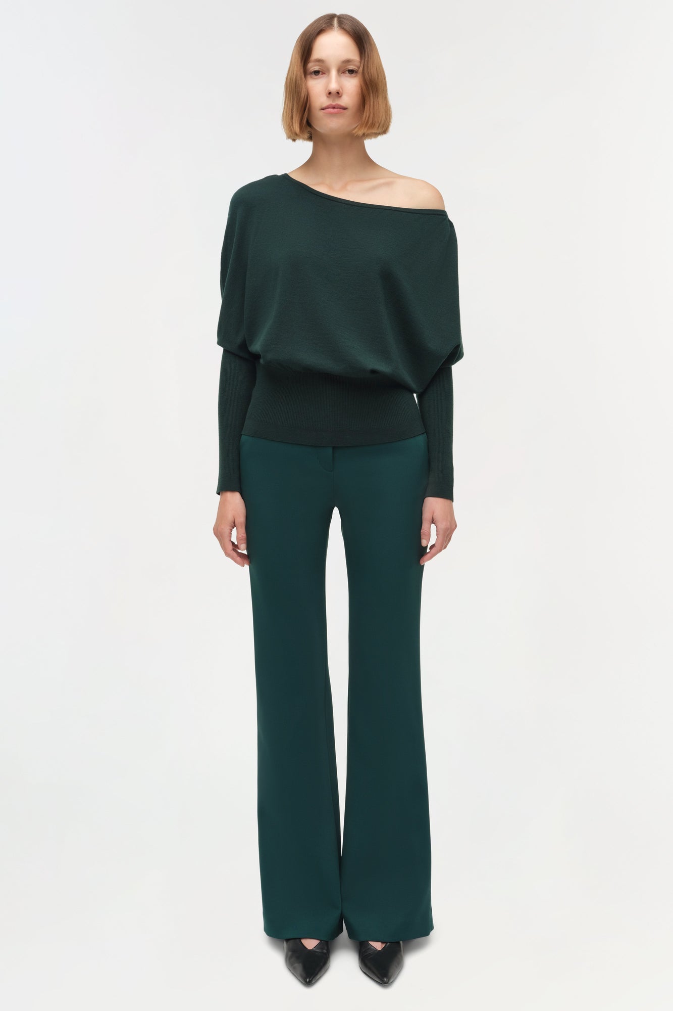 Dark green off-shoulder sweater with draped long sleeves worn with matching flared pants.