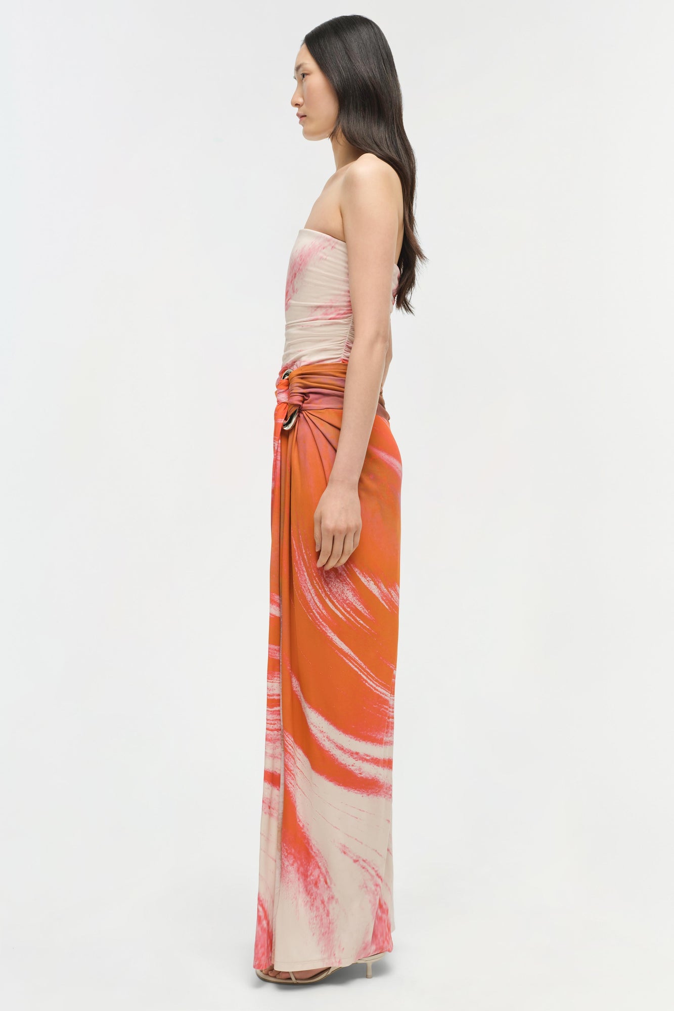Strapless gown with ruched beige and pink bodice, orange and pink gradient skirt with abstract print, side cutout detail.