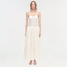Woman wearing cream strapless dress with lace bodice and pleated skirt, paired with beige sandals.