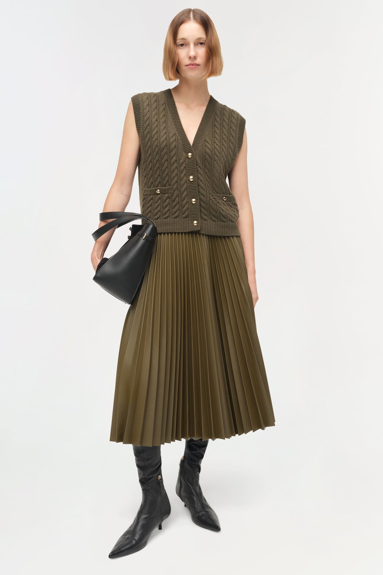 Olive green cable-knit vest with v-neck, button front, and ribbed trim worn over matching pleated skirt.
