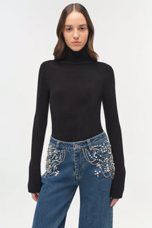 Blue denim crop jeans with rhinestone embellishments on the pockets and waistband, worn with a black turtleneck.
