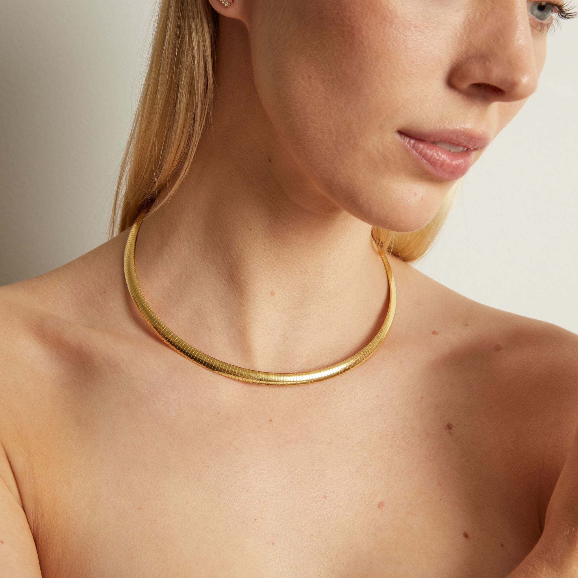 Model. Close-up of a woman wearing a gold necklace against a neutral background