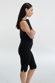 Woman wearing a black sleeveless top and capri leggings on a white background