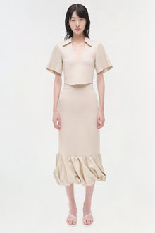 Beige linen knit midi skirt with gathered hem, worn with matching short-sleeve crop top and pink sandals.