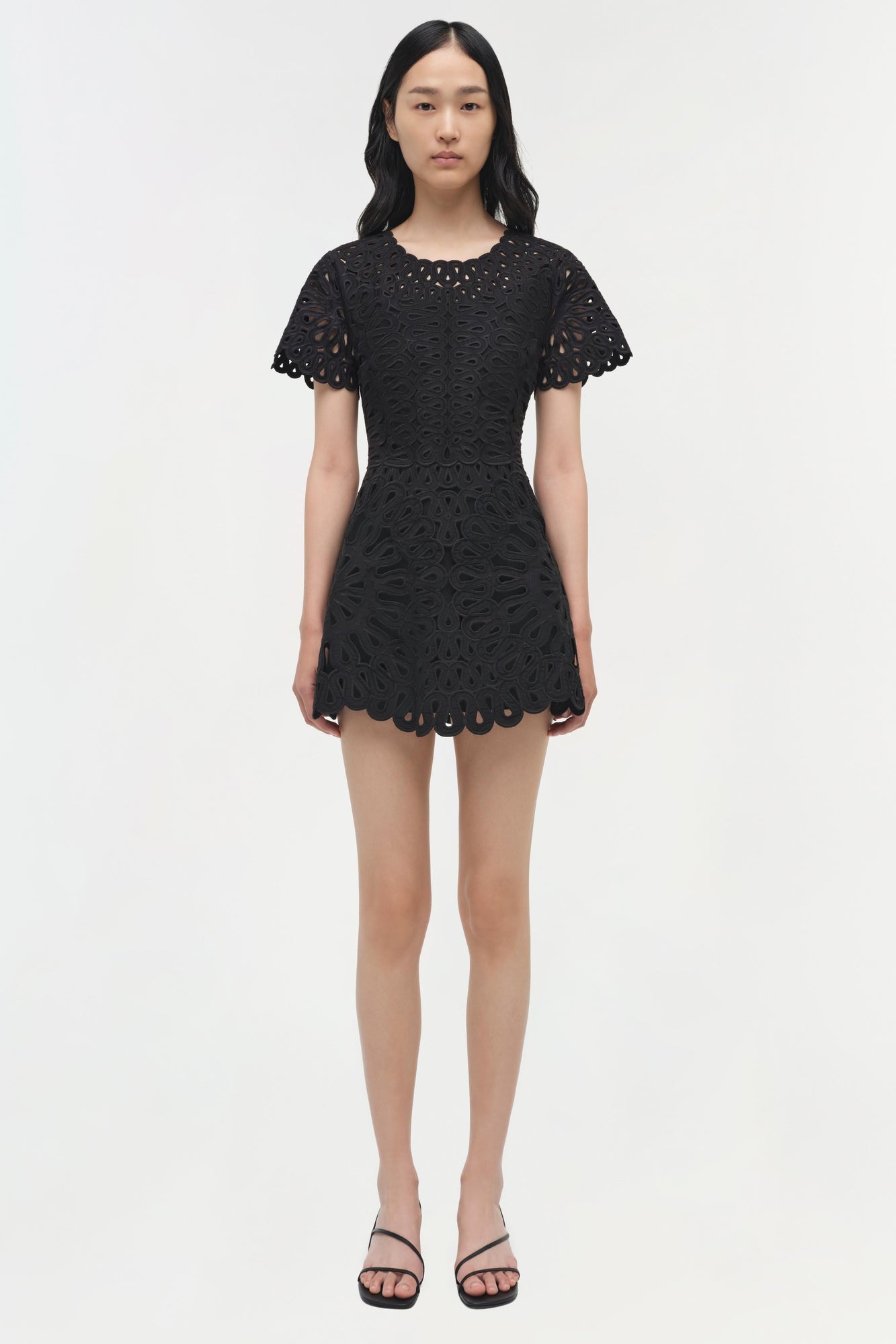 Black mini dress with intricate cutout embroidery throughout, short scalloped sleeves, and scalloped hem.