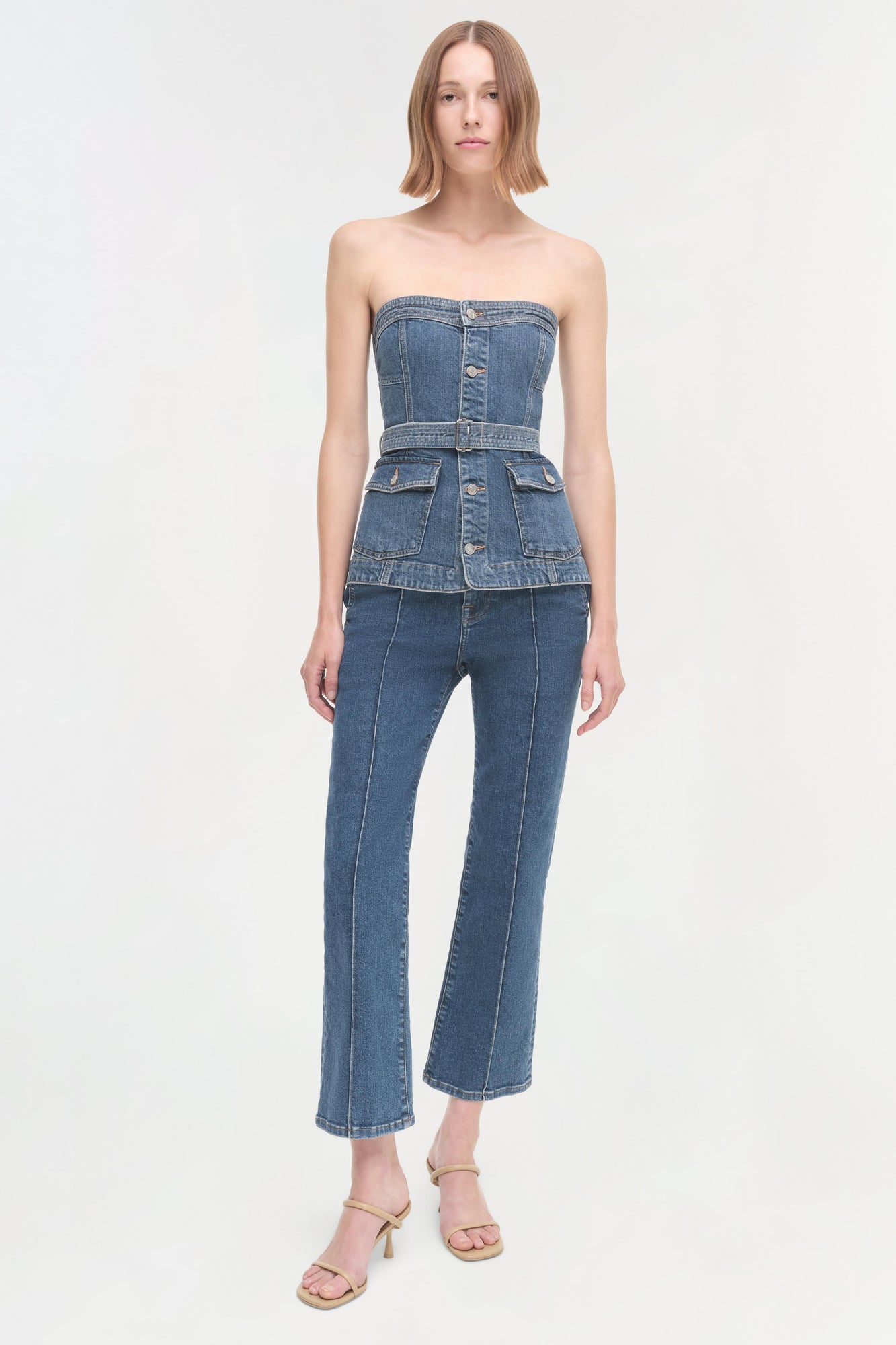 Woman wearing a strapless denim corset top with a waistband and cropped flared jeans.