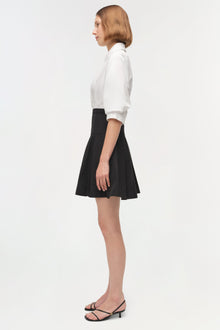 Woman wearing white collared shirt and black A-line mini skirt with black strappy heeled sandals.