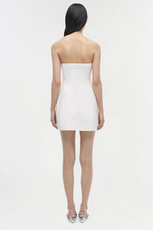 Woman wearing white strapless mini dress, viewed from back, with silver pointed-toe heels.