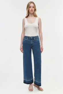 Woman wearing white sleeveless tank top and medium wash wide-leg cropped jeans with darker hem detail.