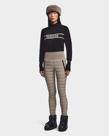 A woman faces forward wearing the Rudsak ARIL M - 8522514 Cement sweater, a fur hat, chic womens quilted pants with side zippers, and black boots against a plain white background.