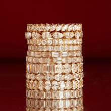 Flatlay Model A tall stack of mixed-cut gold and diamond eternity rings on a dark red background