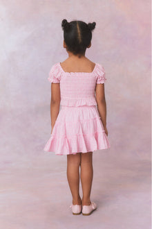 Pink gingham cotton off the shoulder top with puff sleeves and a smocked bodice flowing to a peplum finish for girls.