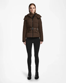 A woman faces forward wearing the Rudsak ADELINE - 8124544 Mocha quilted short down puffer jacket with a belt, paired with black leggings and black ankle boots against a plain white background.