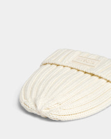 A close-up of the Rudsak ANISA - L423500 Optic White ribbed knit beanie with a rectangular patch on the turned-up brim, perfect for elevating your winter wardrobe. Shown folded on a plain light background.