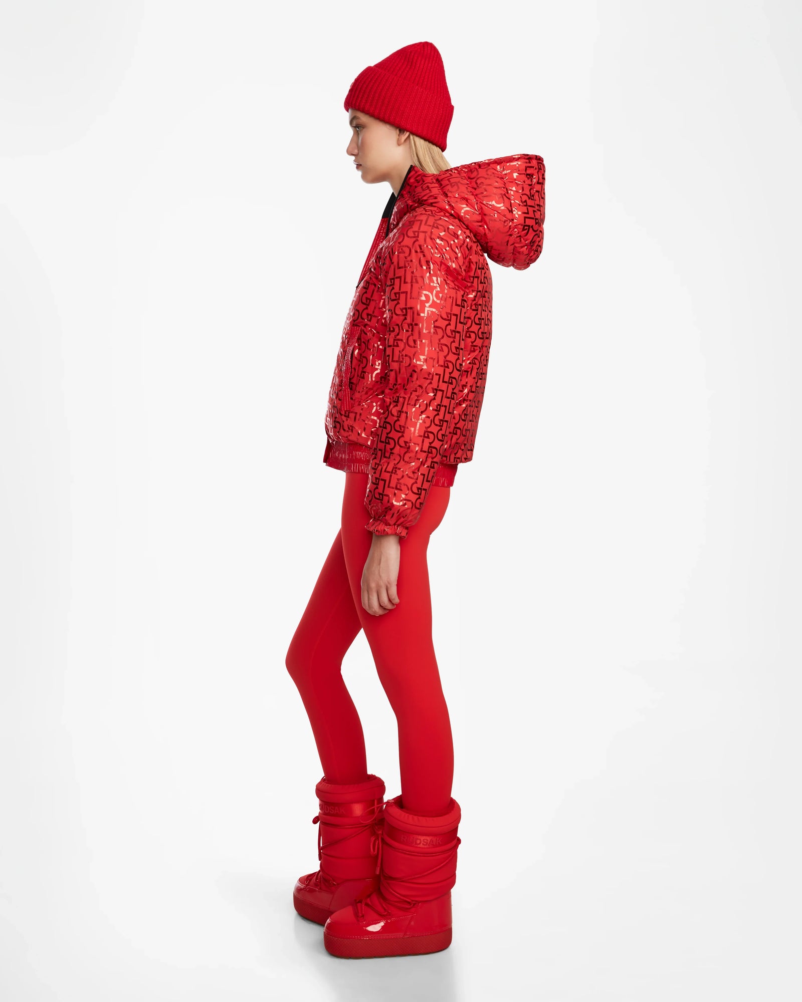 A person in profile wears the Rudsak DANI M - 8124539 Flame Red jacket, paired with red leggings and puffy boots, set against a plain white background.