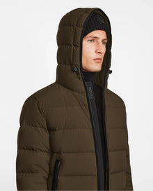 A man wearing the Rudsak DEMIAN M - M123507 Army men’s down puffer jacket with a hood, made from sustainable recycled fabric, and a black knit beanie, looks slightly to the side against a plain white background.