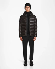 A man faces forward wearing the Rudsak DEMIAN S - M123508 Black mens down puffer, paired with a black beanie, black pants, and boots against a plain white background.