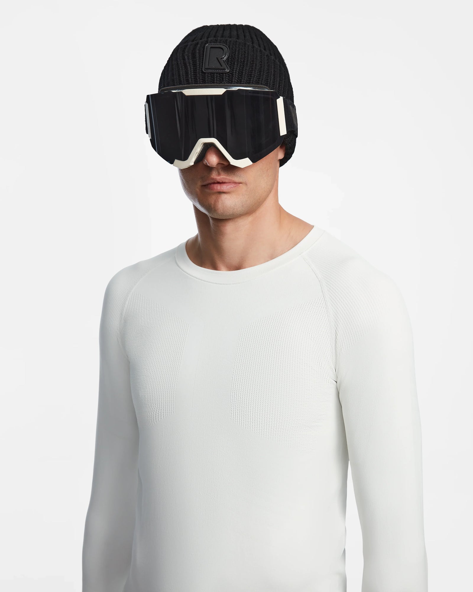 A person models the Rudsak FRANC - 6524541 Iceland, featuring a black beanie, black ski goggles, and a fitted white stretch base layer, standing against a plain white background.