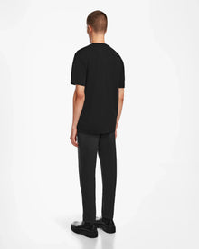A man with short hair faces away, wearing the GIANNI - 6524535 Black mens t-shirt by Rudsak, paired with dark gray pants and black shoes against a plain white background.