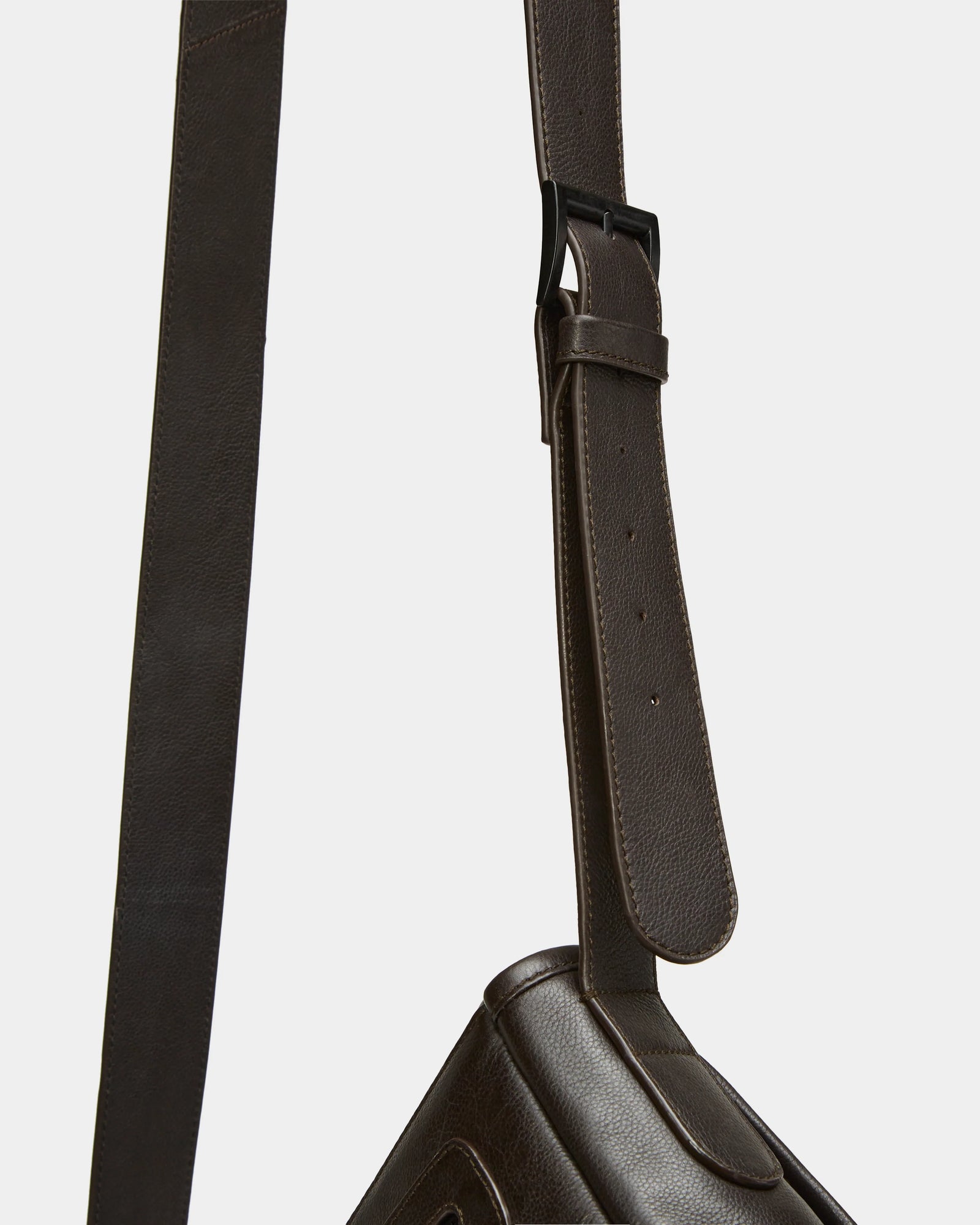 Close-up of the adjustable shoulder strap on the Rudsak GRAYSON - 8324512 Espresso leather crossbody bag, showing its black metal buckle and multiple adjustment holes against a plain white background.