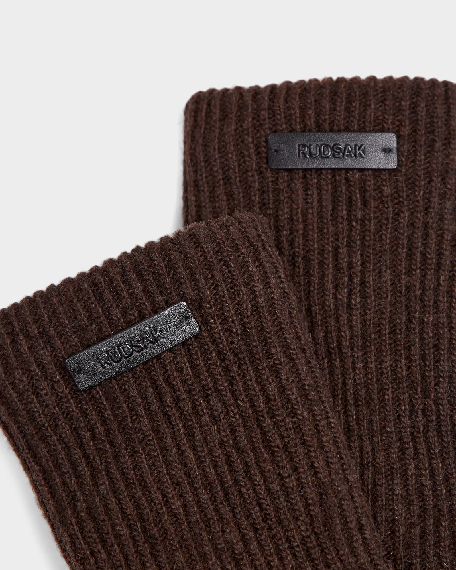 Close-up of two espresso ribbed knit MARINE - 8424516 items by Rudsak, each with a small black rectangular label—perfect for pairing with wool-lined or women’s leather gloves.