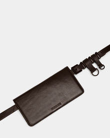 The Rudsak PREYA - 8324508 Espresso is a black leather belt bag with a rectangular pouch, minimal stitching, discreet embossed logo, and an adjustable strap with metal buckles and rings. It’s displayed against a plain light background.