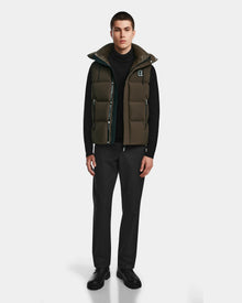 A man faces forward against a white background wearing the Rudsak REN M - 9123512 Army M weather-resistant puffer vest over a black turtleneck, black trousers, and black shoes.