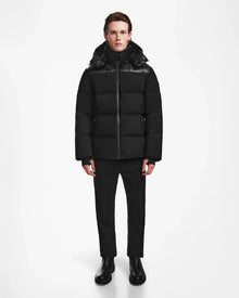 A person faces forward in a Rudsak THEO - M125531 Black weather-resistant men’s down puffer jacket, paired with black pants and boots, set against a white background.