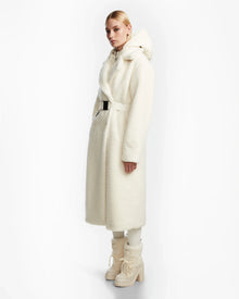 A person poses against a white background wearing the Rudsak TINA - 8123578 Iceland womens faux fur teddy trench coat with a belt, styled with matching boots and light-colored pants.