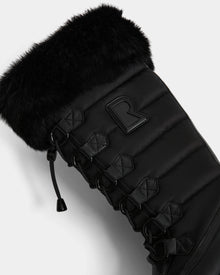 Close-up of the Rudsak WINDY - L224507 Black women's winter boot, featuring faux fur trim, quilted stitching, black laces with metal eyelets, and a raised R logo. Padded fabric offers extra warmth and comfort for cold weather.