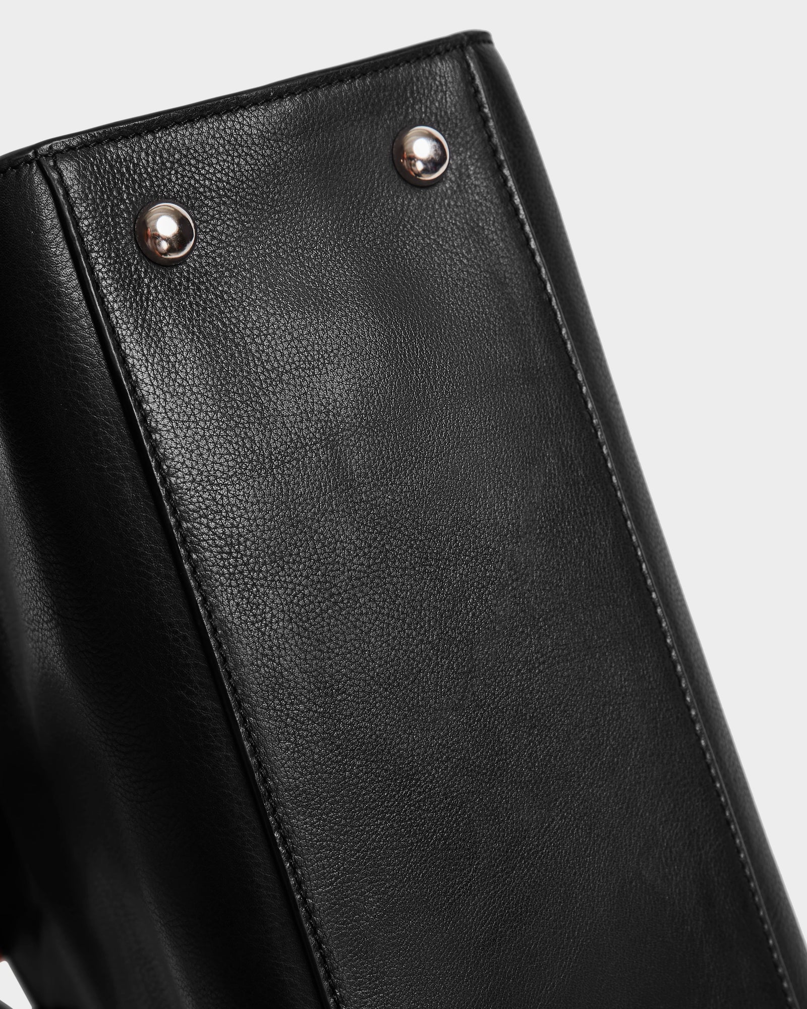 Close-up of the bottom of the Rudsak YASMINA - 8324527 Black womens leather tote bag, featuring two metal studs, set against a plain light background.