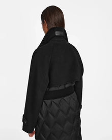 A person with straight brown hair is seen from behind wearing the Rudsak ZOE - 8124711 Black womens long trench coat with a high collar and quilted lower section, set against a plain white background.