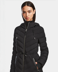 A woman with straight dark hair wears the Rudsak FRANCINE - 8124722 Black puffer jacket, featuring RDS-certified down, a front zipper, and drawstring waist, standing against a plain white background.