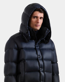 A man wears the BRAYDEN S - M125525 Navy quilted down puffer jacket by Rudsak with the hood up, looking slightly to the side against a plain light background.