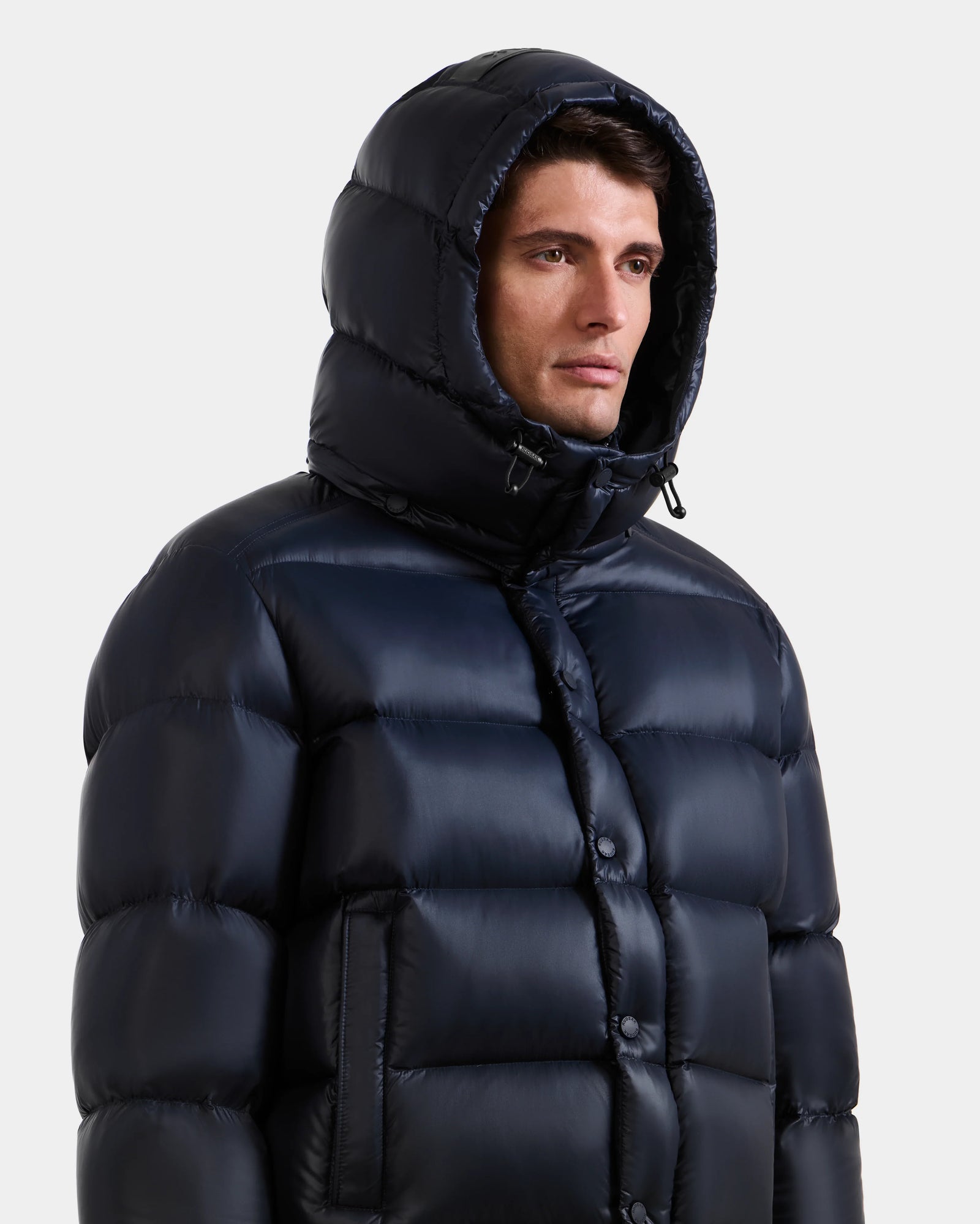 A person wears the Rudsak BRAYDEN S - M125525 navy down puffer jacket with hood up, looking slightly to the side against a plain light background.
