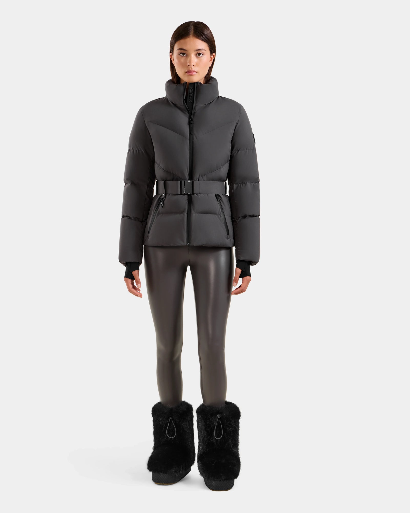 A woman stands facing forward in the CHRISTELLE M - L125542 Grey quilted down puffer jacket by Rudsak, shiny black leggings, and black furry boots against a plain white background.