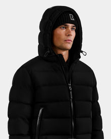 A man wearing the Rudsak DEMIAN M - M123507 Black down puffer jacket and a black beanie with a white 