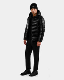 A man faces forward against a light gray background wearing the Rudsak DEMIAN S-R - M123505 Black men’s down puffer jacket with RDS-certified down, paired with a black beanie, pants, and boots.
