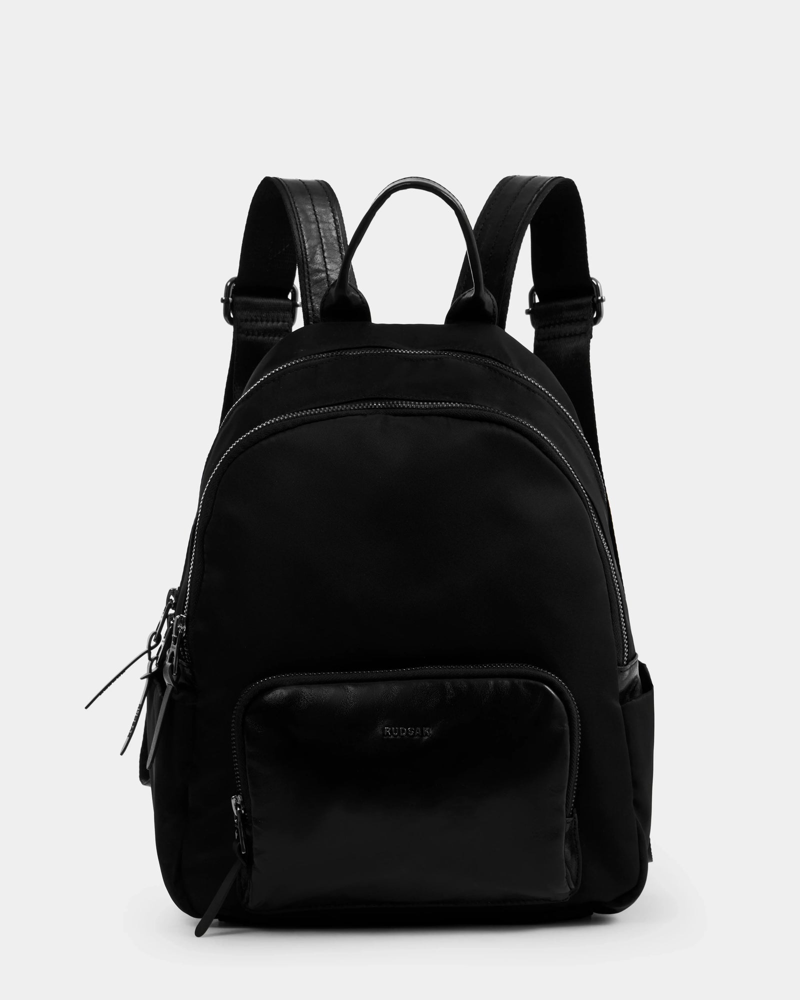 The Rudsak GRACE - L325013 Black women’s mini backpack is made from lightweight technical fabric with silver zippers, a front zip pocket, two side pockets, and adjustable padded straps—an ideal city-ready essential.