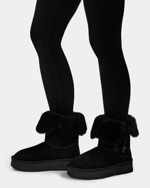 A person models Rudsak’s INESA - L225026 Black suede platform boots with cozy wool lining and black leggings, standing against a plain light background, legs and feet visible.