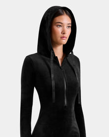 A woman wears the Rudsak ISABELLA - L525502 Black fitted zip-up hoodie with its crystal-sequin logo and hood up, gazing slightly to the side against a plain light background.