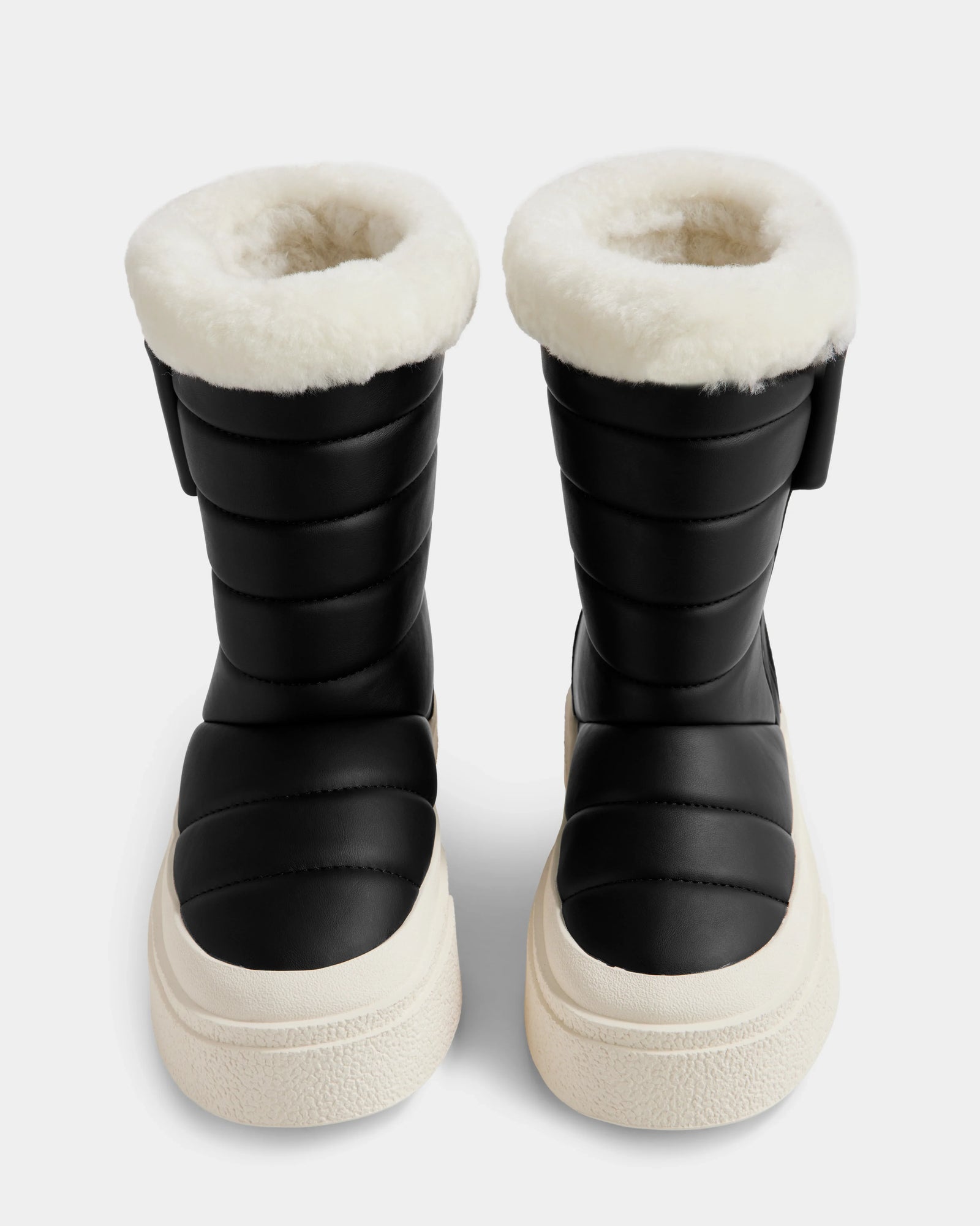 The Rudsak KATHIE - L225516 Black vegan leather winter boots feature thick white fur lining and chunky white soles, displayed front-facing on a plain light background.